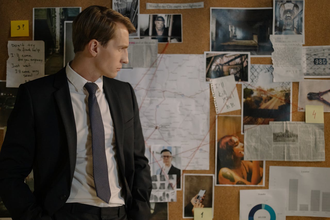 Detective in suit examining evidence on cork board during investigation process.